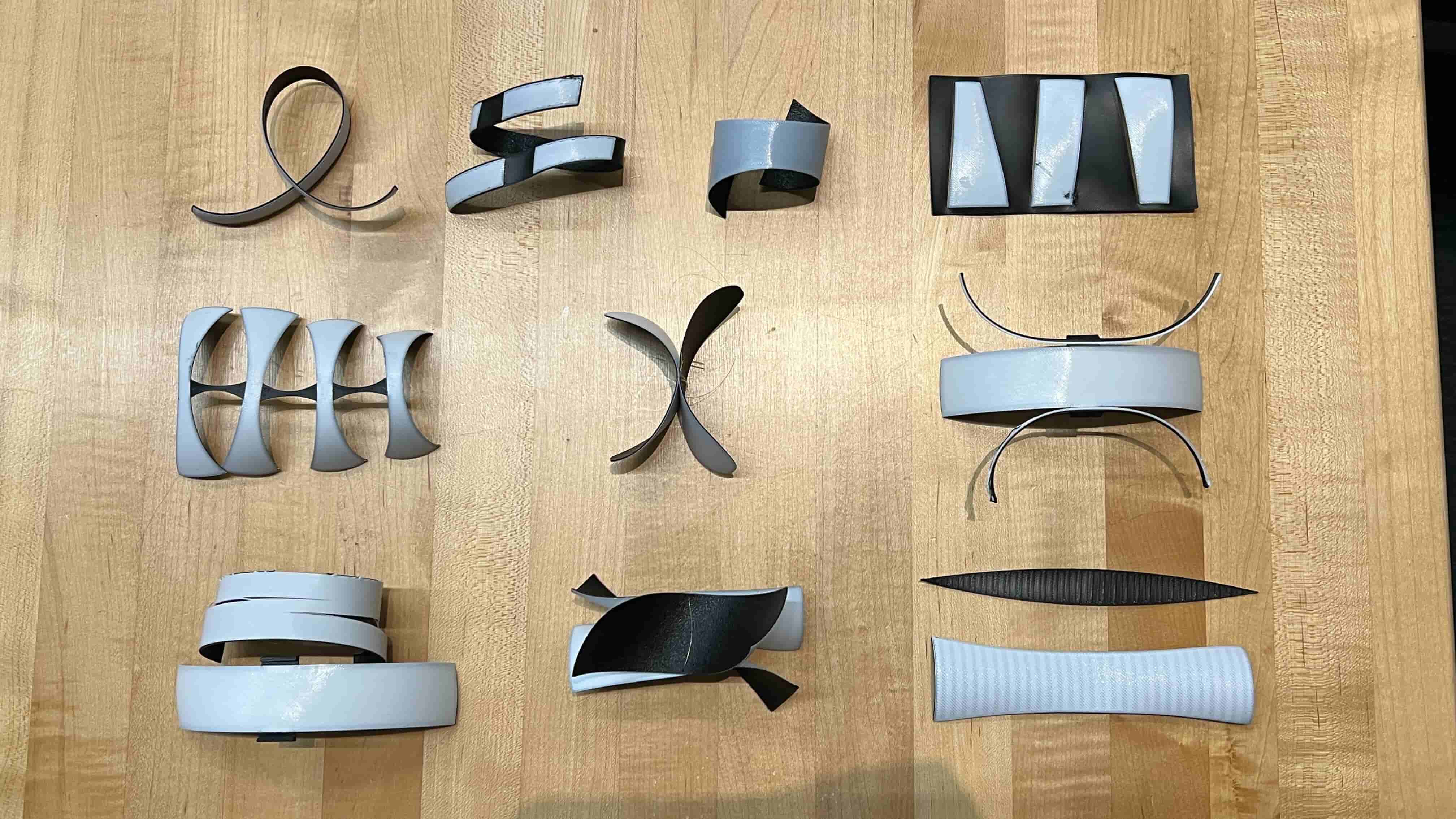 Three rows of '4D printing' experiments showing white PLA and black TPU patterns on wooden background